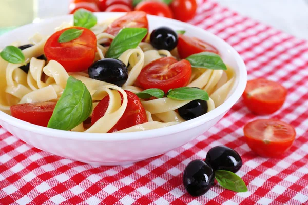 Spaghetti with tomatoes, olives and basil leaves on plate on fabric background — Stock Photo, Image