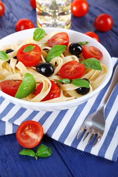 Spaghetti con pomodori, olive e foglie di basilico su piatto su tovagliolo su fondo di legno — Foto Stock
