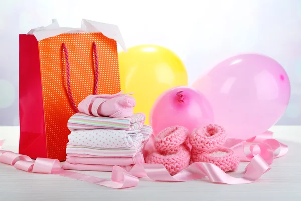Ropa de bebé y bolsa de regalo sobre fondo brillante —  Fotos de Stock
