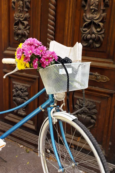 Altes Fahrrad mit Blumen im Metallkorb auf braunem Türhintergrund — Stockfoto