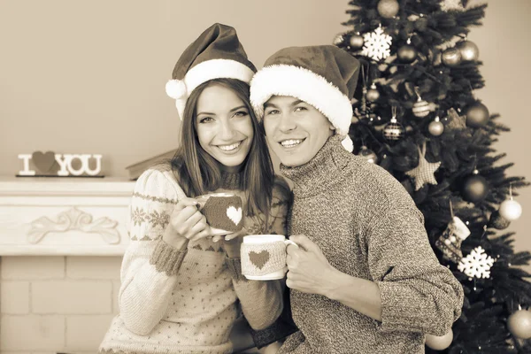 Bom casal de amor sentado com canecas na frente da lareira perto da árvore de Natal. Mulher e homem celebrando o Natal — Fotografia de Stock