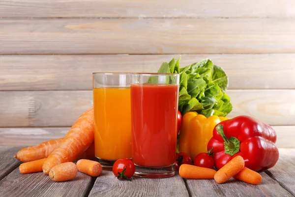 Морковь и томатный сок в стаканах и свежие овощи на деревянном столе на фоне стен — стоковое фото