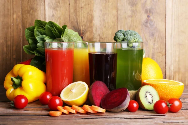 Suco de frutas e vegetais em copos e frutas e legumes frescos na mesa de madeira no fundo da parede de madeira — Fotografia de Stock