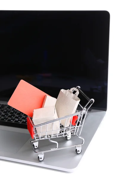 Bolsas de compras y tarjeta de crédito en el carrito de la compra en el ordenador portátil aislado en blanco — Foto de Stock