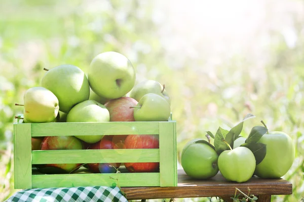 Juicy apples in wooden box on grass, outdoors — Stock Photo, Image