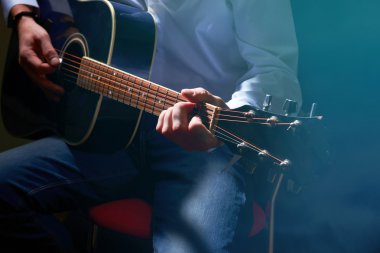 Young musician playing acoustic guitar on dark background clipart