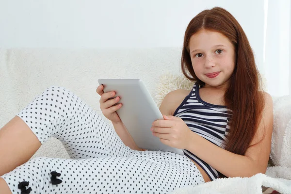 Schönes kleines Mädchen mit Tablet auf dem Sofa im Zimmer — Stockfoto