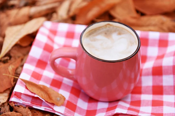 Beker van lekkere warme drank op servet, op herfst bladeren achtergrond — Stockfoto
