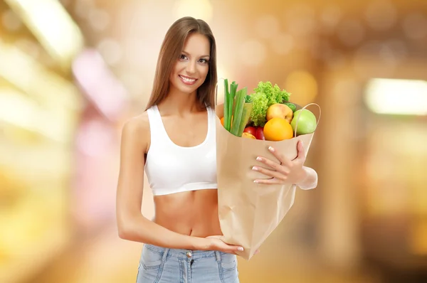 Winkelen concept. Mooie jonge vrouw met groenten en fruit in boodschappentas op winkel achtergrond — Stockfoto