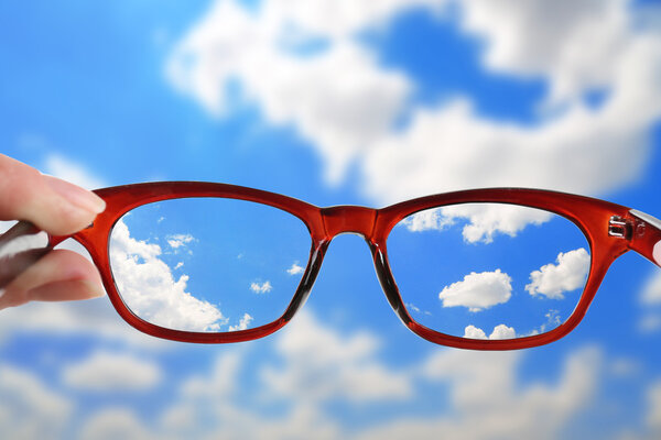 Концепция видения. Очки в руке на фоне неба
