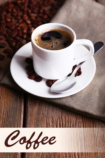 Cup of coffee and coffee beans on napkin on wooden background — Stock Photo, Image