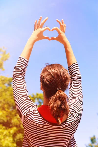 Ung flicka håller händerna i hjärtat formen inramning på blå himmel bakgrund — Stockfoto
