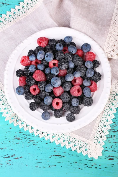 Ледяные ягоды на тарелке, на цветном деревянном фоне — стоковое фото