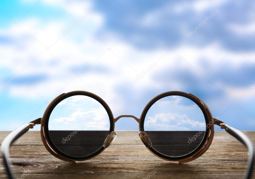 Vision concept. Glasses on wooden table and sky background