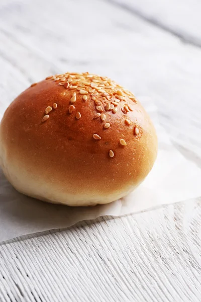 Tasty bun with sesame on color wooden background — Stock Photo, Image