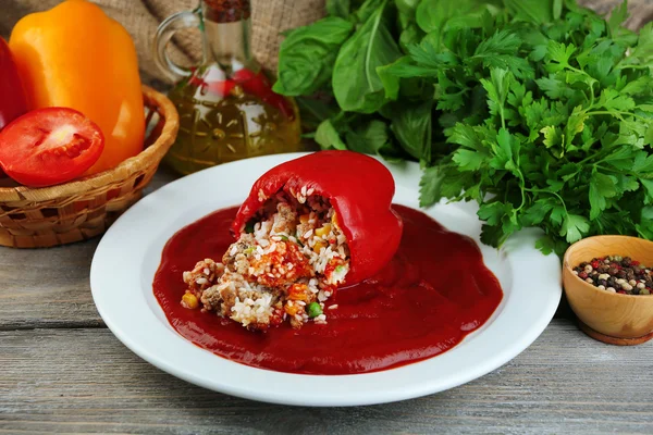 Prepared stuffed pepper with tomato sauce on plate, on wooden background — Stock Photo, Image