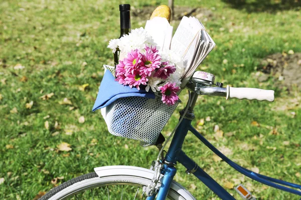 Bicicleta con flores, pan y botella de vino en canasta de metal sobre fondo de hierba —  Fotos de Stock