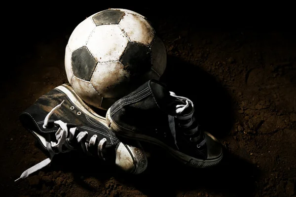 Futbol topu ve spor ayakkabılar topraklarında — Stok fotoğraf