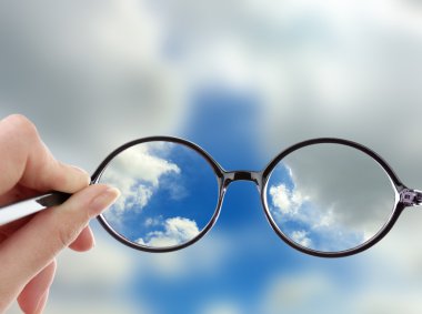 Glasses in hand on sky background