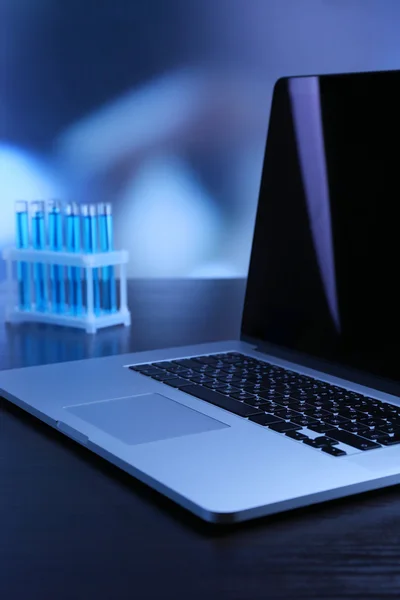 Ноутбук с пробирками в лаборатории на синем фоне — стоковое фото