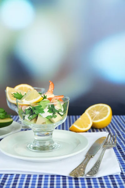 Tasty salads with shrimps and avocado in glass bowl and on plate, on table, on bright background — Stock Photo, Image