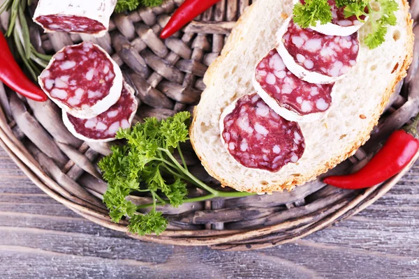 French salami with parsley and chilly pepper on wicker mat on wooden background — Stock Photo, Image