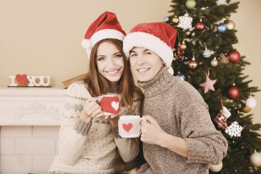 Güzel aşk çift kupalar Noel ağacı yakınındaki şömine önünde oturuyor. Kadın ve adam Noel Kutlamaları