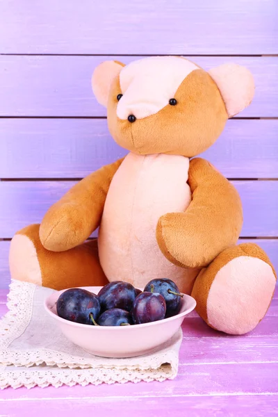 Toy bear and bowl of plums — Stock Photo, Image