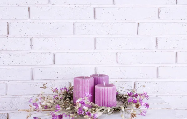 Lila kaarsen en gedroogde bloemen op bakstenen muur achtergrond — Stockfoto