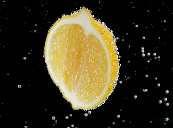 Lemon segar dalam air dengan gelembung pada latar belakang hitam — Stok Foto