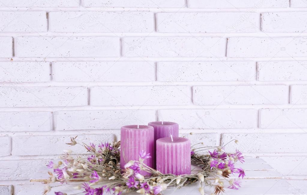 Lilac candles and dried flowers on brick wall background