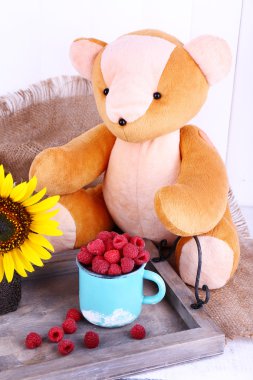 Oyuncak ayı ve ahududu ahşap tepsi üzerinde çul ahşap duvar arka plan üzerine bir fincan