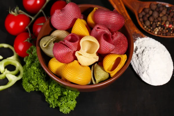 Composizione di pasta colorata in ciotola, pomodori freschi, prezzemolo su fondo di legno scuro — Foto Stock