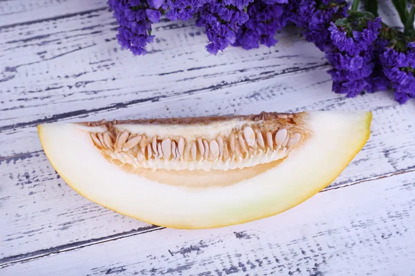 Slice of melon on plate and flowers on wooden background — Stock Photo, Image