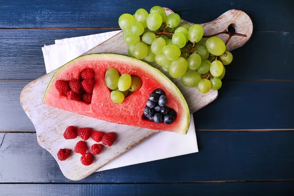 Fresh juicy watermelon slice  with cut out heart shape, filled fresh berries, on cutting board, on color wooden background — Stock Photo, Image