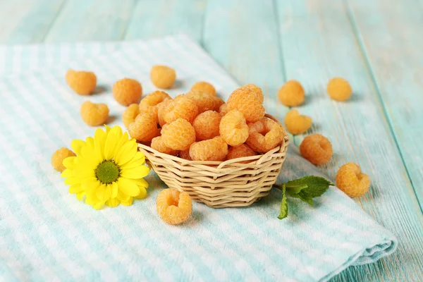 Yellow raspberries in basket and wildflower on checkered napkin on wooden background — Stock Photo, Image