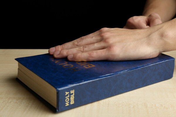 Male hands with Bible on wooden table on dark background