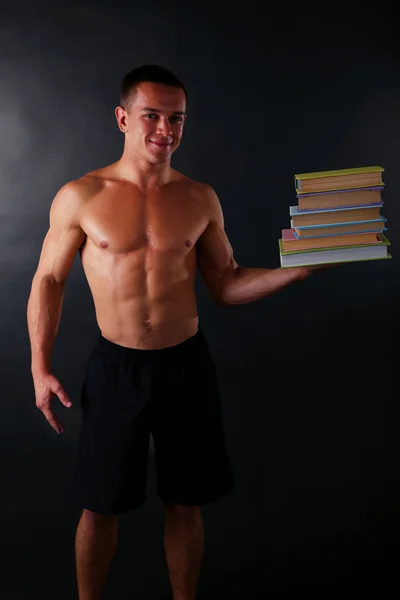 Yakışıklı kas genç adam koyu arka plan üzerine kitaplar teslim — Stok fotoğraf