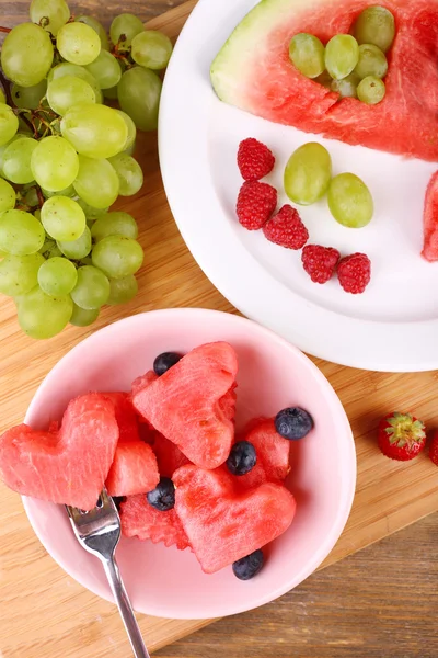 Fresh juicy watermelon slice  with cut out heart shape, filled fresh berries, on plate, on wooden background — Stock Photo, Image