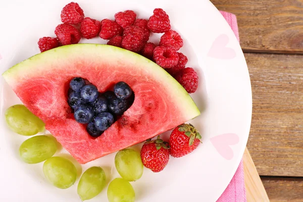 Fresh juicy watermelon slice  with cut out heart shape, filled fresh berries, on plate, on wooden background — Stock Photo, Image