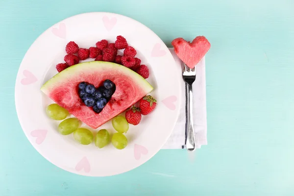 Fresh juicy watermelon slice  with cut out heart shape, filled fresh berries, on plate, on wooden background — Stock Photo, Image