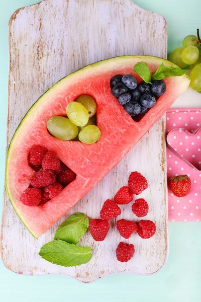 Fresh juicy watermelon slice  with cut out heart shape, filled fresh berries, on cutting board, on wooden background — Stock Photo, Image