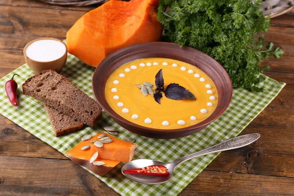 Sopa de calabaza en plato de color y rebanada de calabaza en la servilleta, sobre fondo de madera — Foto de Stock