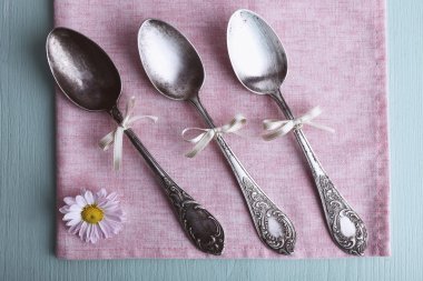 Metal spoons on pink napkin on light blue wooden background clipart