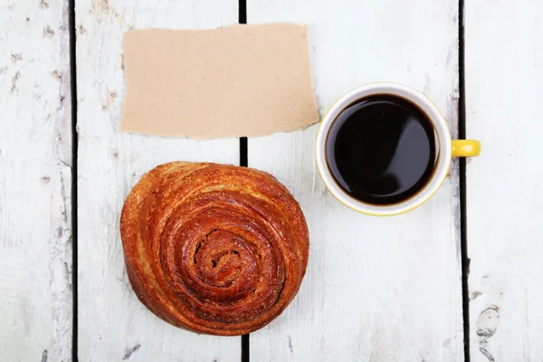 Composición de café, bollo fresco y tarjeta de papel sobre fondo de madera — Foto de Stock