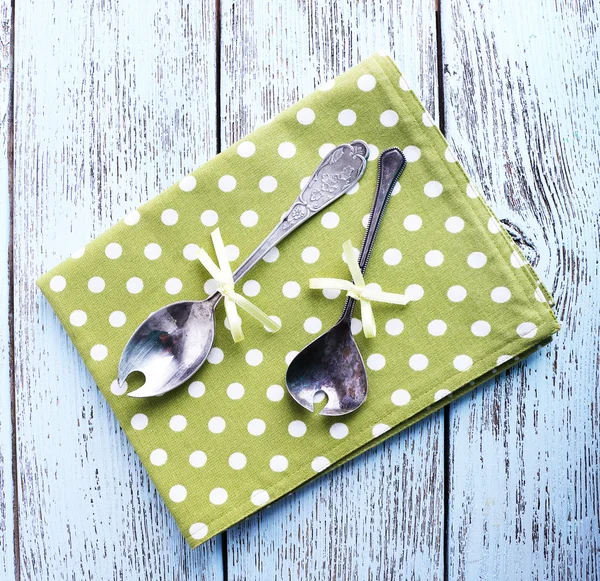 Metal spoons on green polka dot napkin on wooden background — Stock Photo, Image