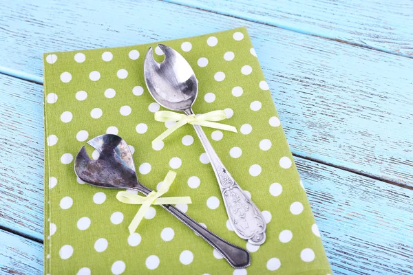 Metal spoons on green polka dot napkin on wooden background — Stock Photo, Image