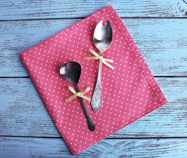 Metal spoons on pink polka dot napkin on wooden background — Stock Photo, Image