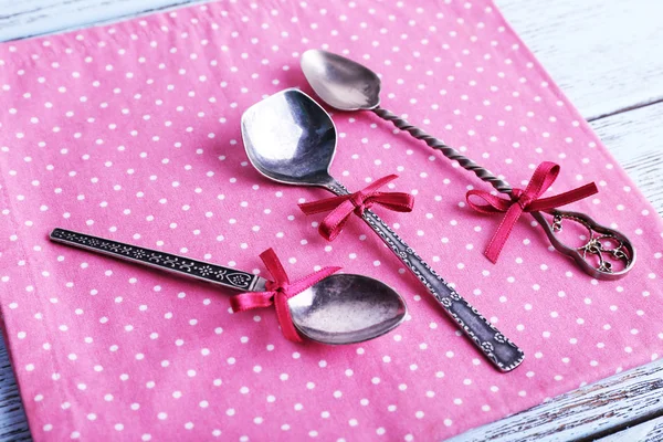 Metal spoons on pink polka dot napkin on wooden background — Stock Photo, Image