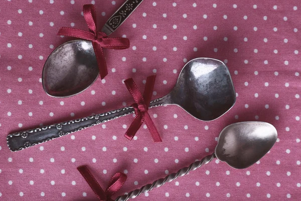 Metal spoons on pink polka dot fabric background — Stock Photo, Image